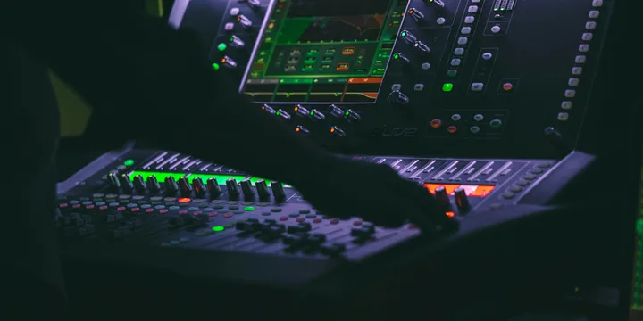 Engineer's hands working faders and knobs on an illuminated digital mixing console.