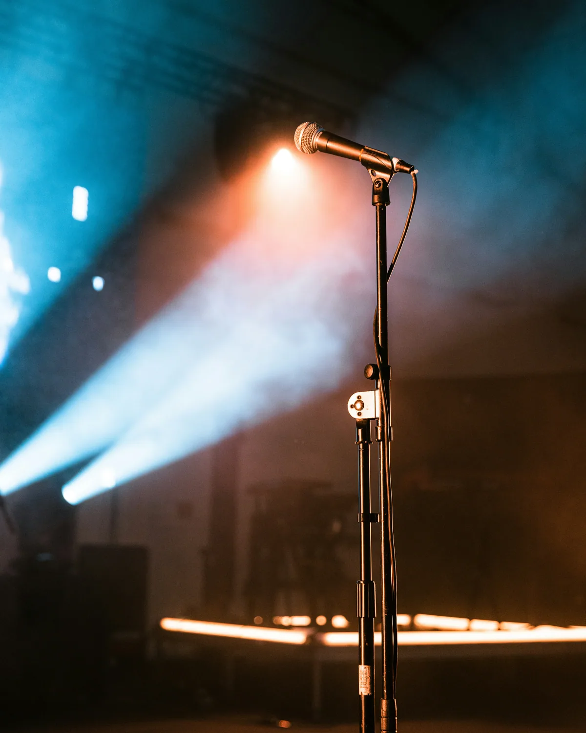 Vocal microphone on a stand under cool stage spotlights at a live show.