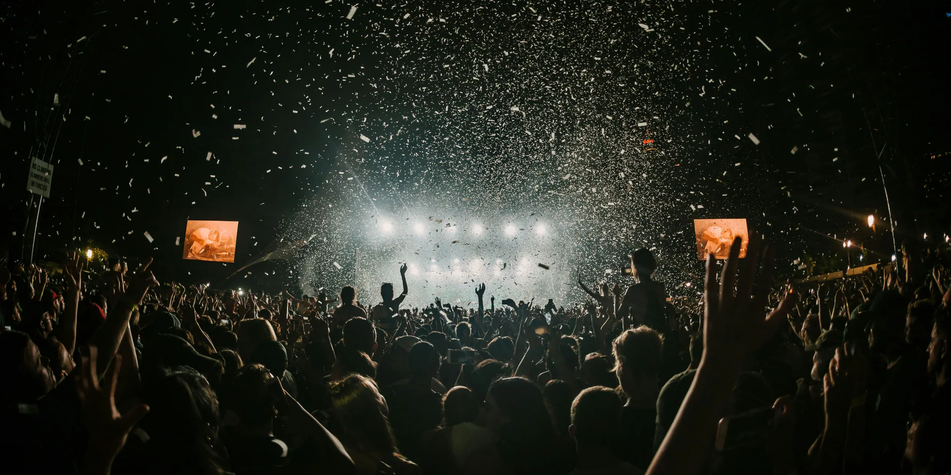 Concert audience under stage lights as confetti fills the arena.