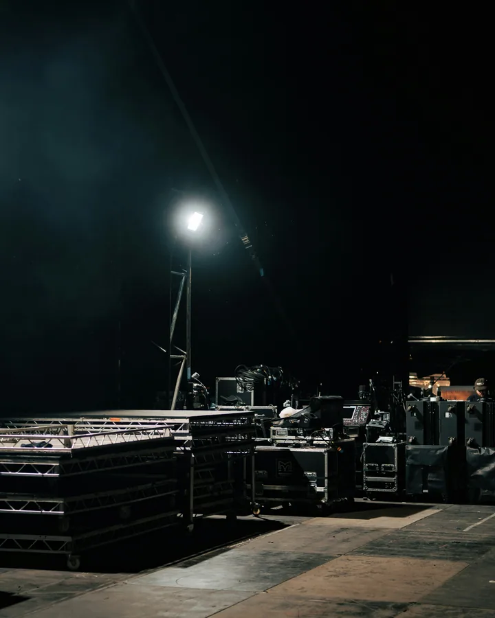 Backstage staging area at night — flightcases, truss, work lights, ready for load-in.