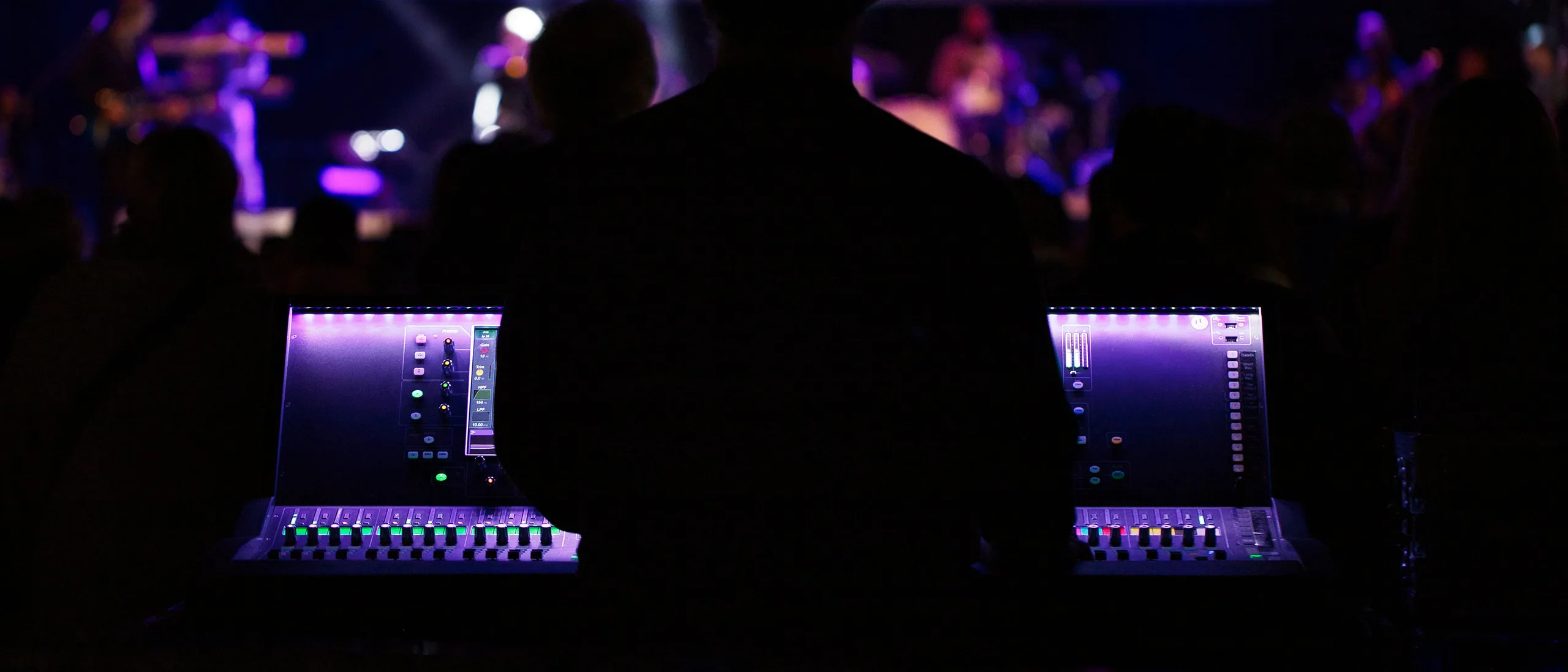 Front-of-house consoles illuminated under stage lights, engineer silhouetted at the desk.
